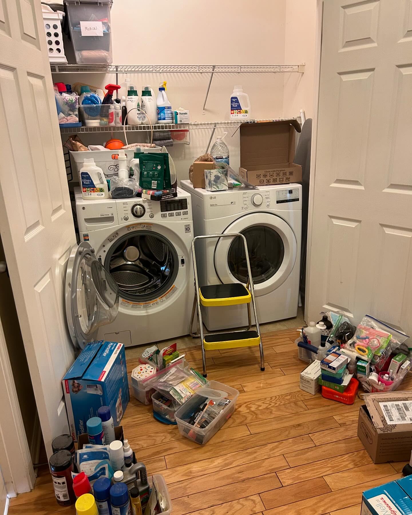 Messy laundry room before organizing — supplies, boxes, and bins piled on the floor around the washer and dryer