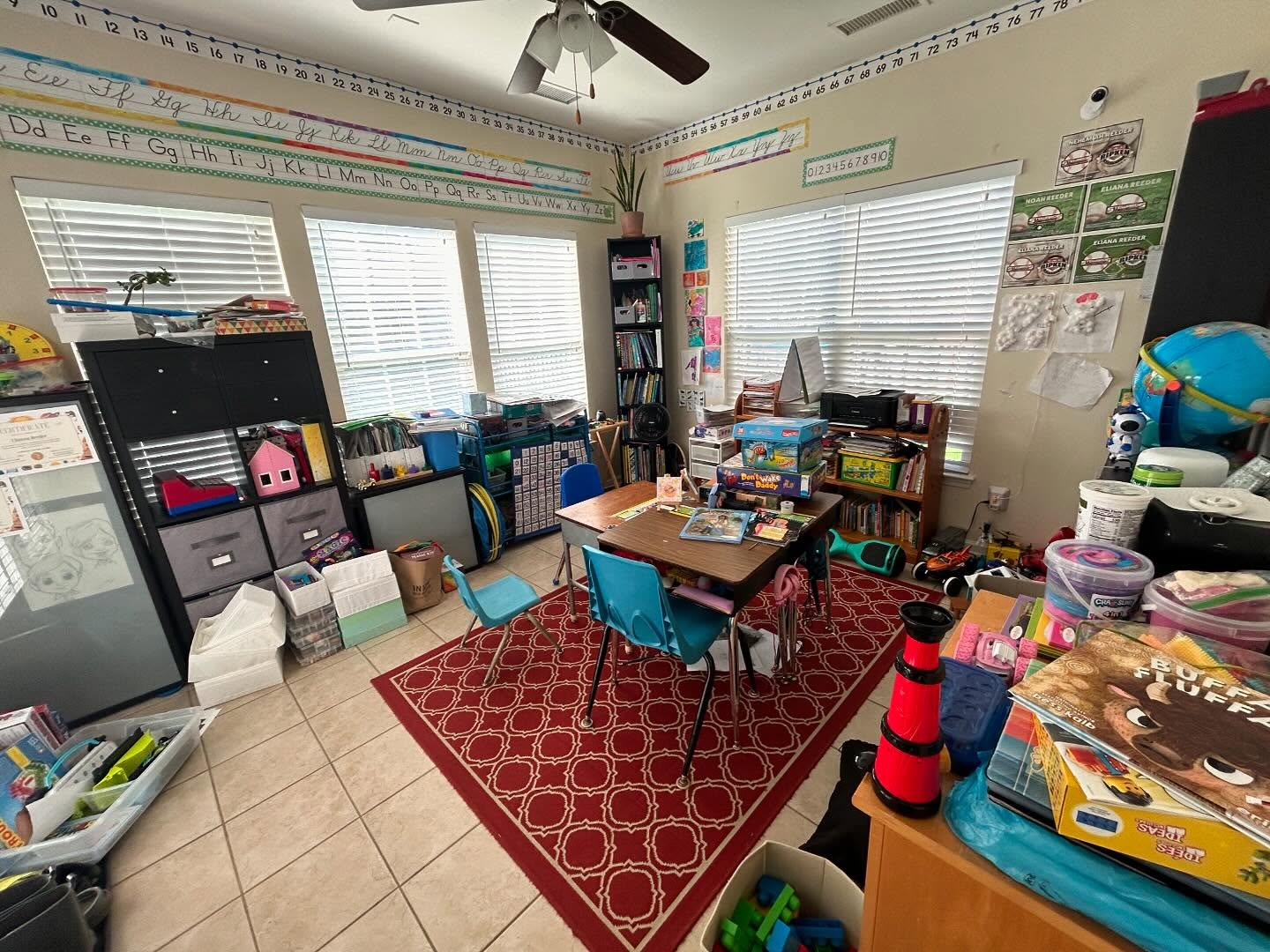 Disorganized homeschool classroom before decluttering — bins, books, and learning materials piled on floor and desks